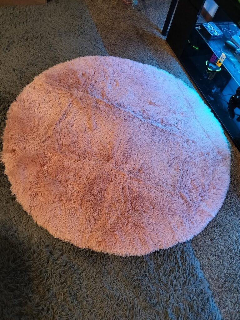 Amazon Basics fluffy washable round area rug in soft pink, high-pile shag texture placed on carpeted living room floor