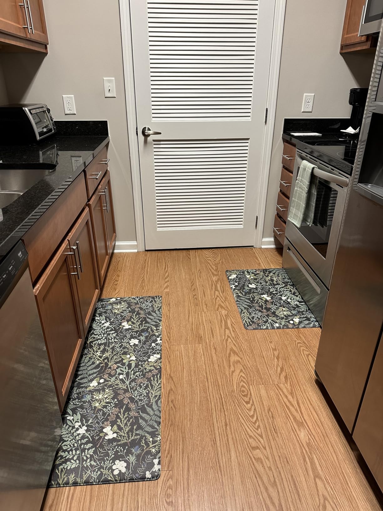 Keensoft botanical kitchen rug set with green and white leaf pattern placed on wooden kitchen floor between cabinets and stove